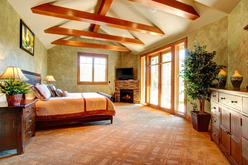 Spanish style bedroom with mattress, nightstand, dresser, indoor plant, exposed ceiling beams, fireplace, and windows