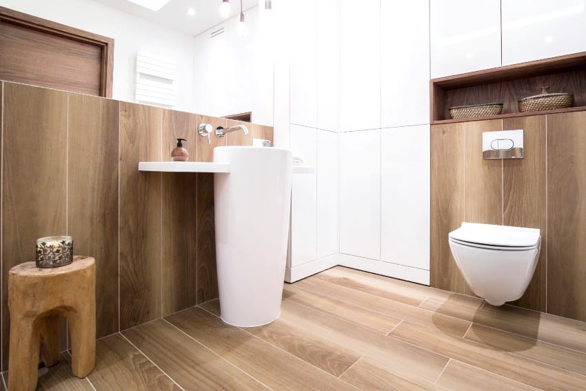 Stunning modern bathroom with white and wooden tones features modern pedestal sink and toilet