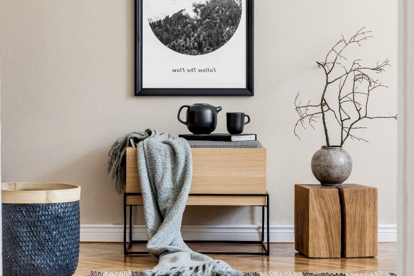 Stylish modern scandinavian living room interior with black mock up poster frame, maple furniture, leaf in vase, black rattan basket, books and elegant accessories