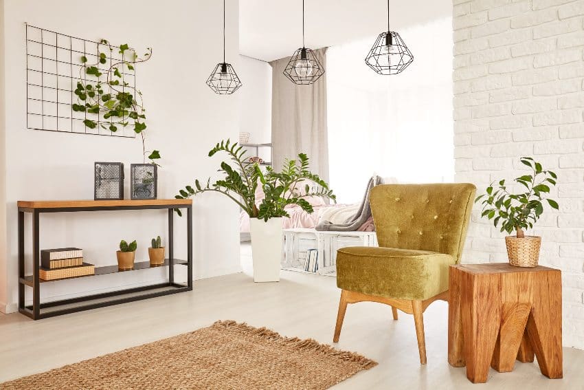 Stylish white room with green armchair and chestnut wood side table, plants, rug and pendant lights