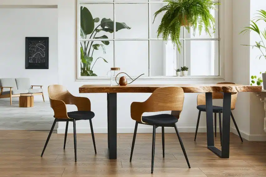 Stylish with a nature vibe interior of dining room with design craft maple wood table and chairs, several plants, big window and elegant accessories in modern home