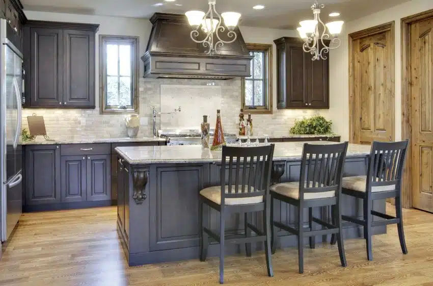 Traditional kitchen interior with wooden floors, dark paint colonial cabinets, island with granite countertops and chairs