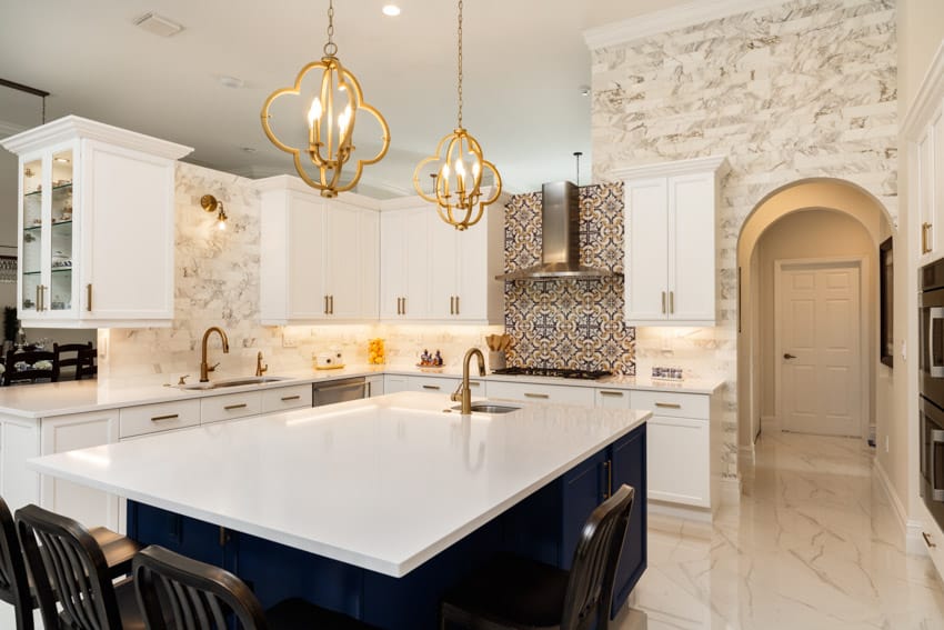 Transitional kitchen with Spanish tile backsplash, island, countertops, white cabinets, sink, faucet, and pendant lights