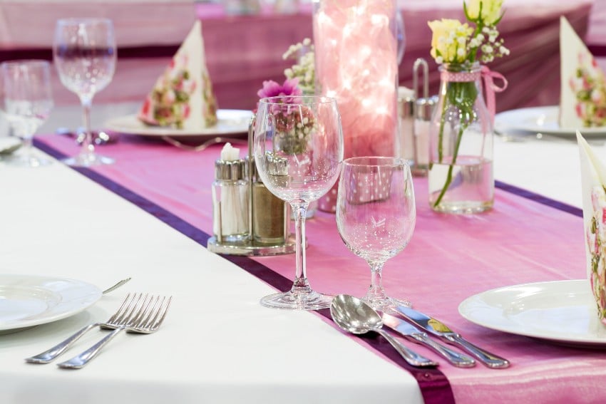 Wedding table set up with glasses, plates, and utensils as well as white and purple organza tablecloth