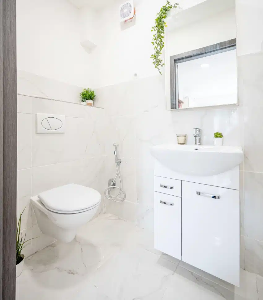 White bathroom features marble floors and walls, pedestal sink with shelving and toilet 