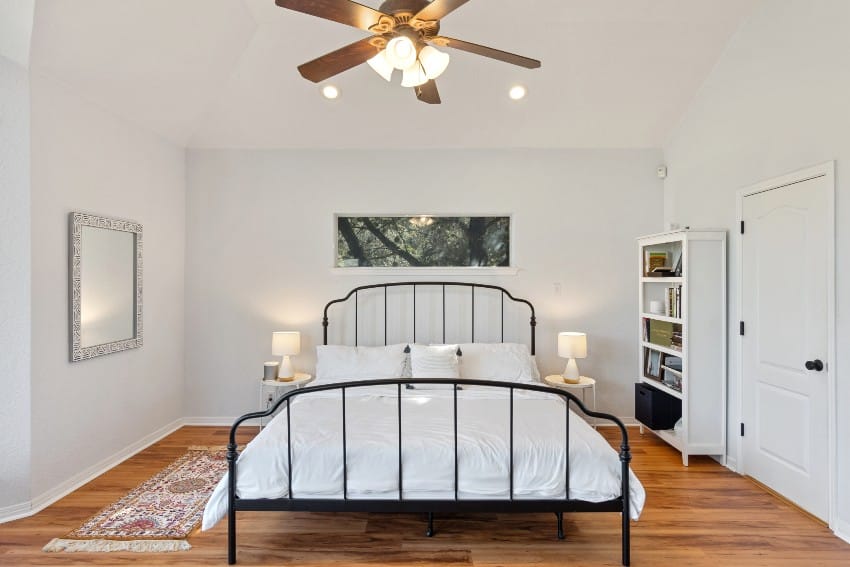 Bedroom with lack wrought iron bed, mirror on the wall and ceiling fan
