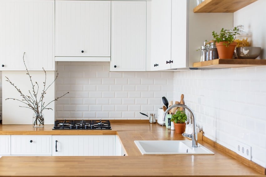 White kitchen in scandinavian style with potted herbs on wood formica counter and white ceramic brick backsplash