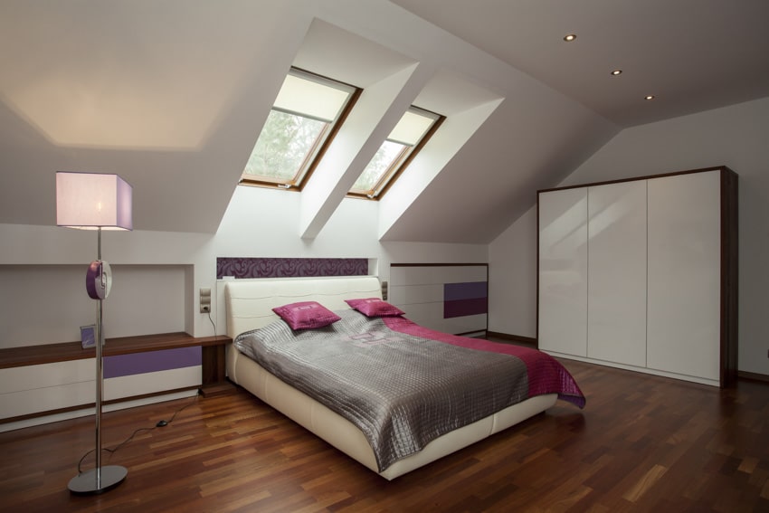 Attic bedroom with floor lamp, skylight window, wardrobe, wood floors, bed, comforter, and pillows
