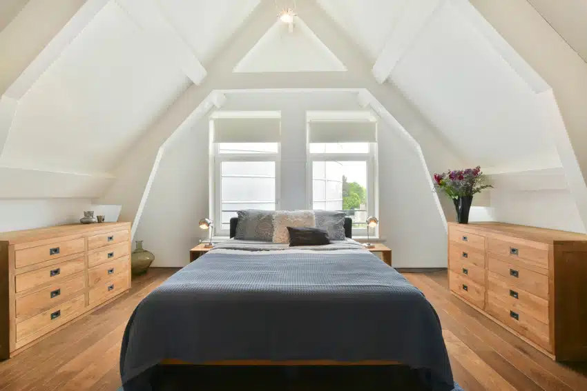 Attic bedroom with mattress, oak wood dressers, windows, and pillows