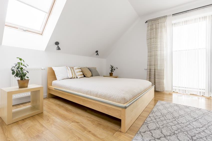 Attic bedroom with oak wood nightstand, bed frame, mattress, skylight, window, and curtains