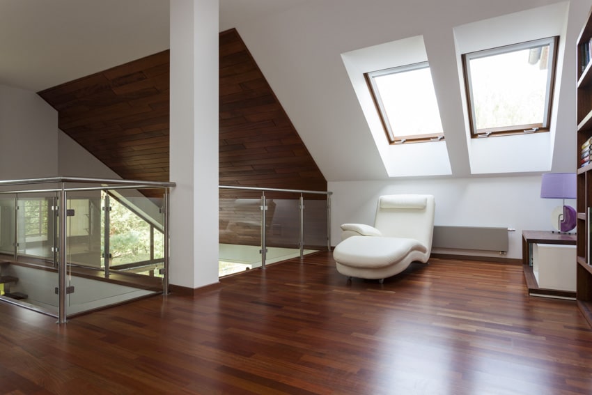 Attic living room with skylight windows, wood floors, accent chair, and bookshelf