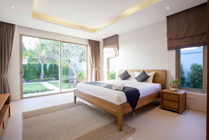 Bedroom with nightstand, mattress, pillows, cove ceiling lighting, windows, and curtains