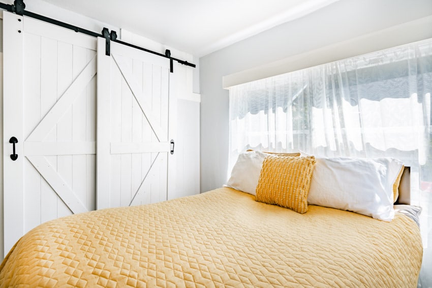 Bedroom with bypass barn door, yellow bedding, pillows, window, and sheer curtains