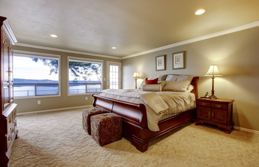 Bedroom with windows, ceiling lights, ottoman pouf, cherry wood nightstands, lamps, footboard, comforter, and pillows