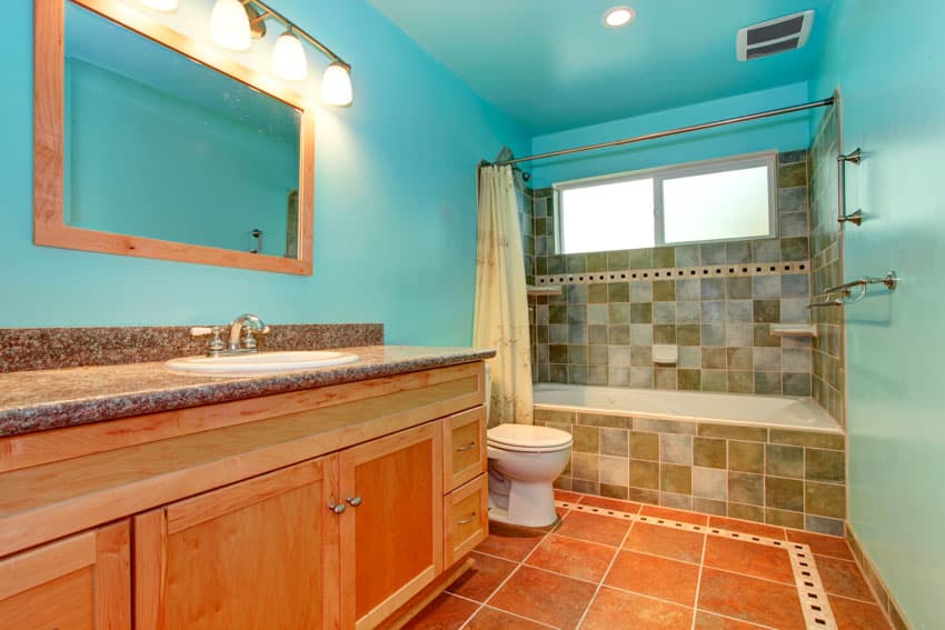 Blue green bathroom with mirror, granite countertop, wood cabinets, tile floor, shower curtain, tile backsplash, and window