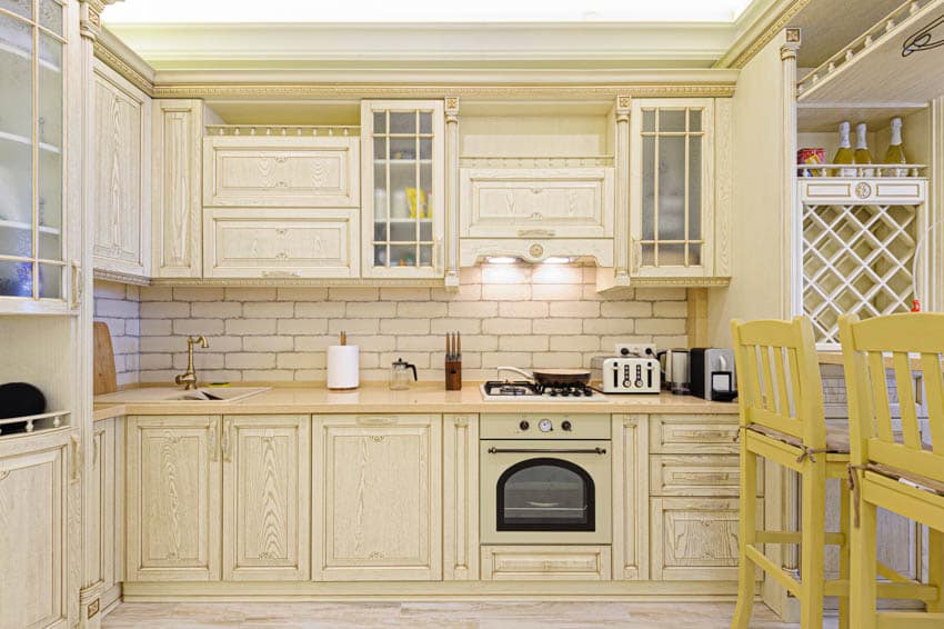 Classic kitchen with subway tile backsplash, oven, range hood, white washed cabinets, and yellow high chairs