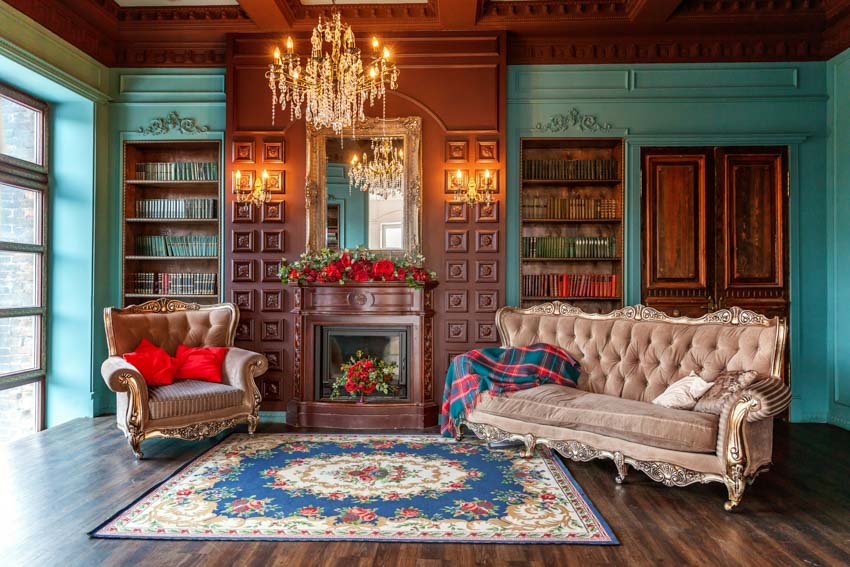 Classic living room with English regency style cushioned chair, sofa, bookshelves, fireplace, wood floor, rug, window, and chandelier