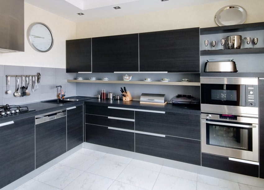 Modern kitchen with floating shelf, countertop, tile flooring, oven, black grain cabinets, and wall clock