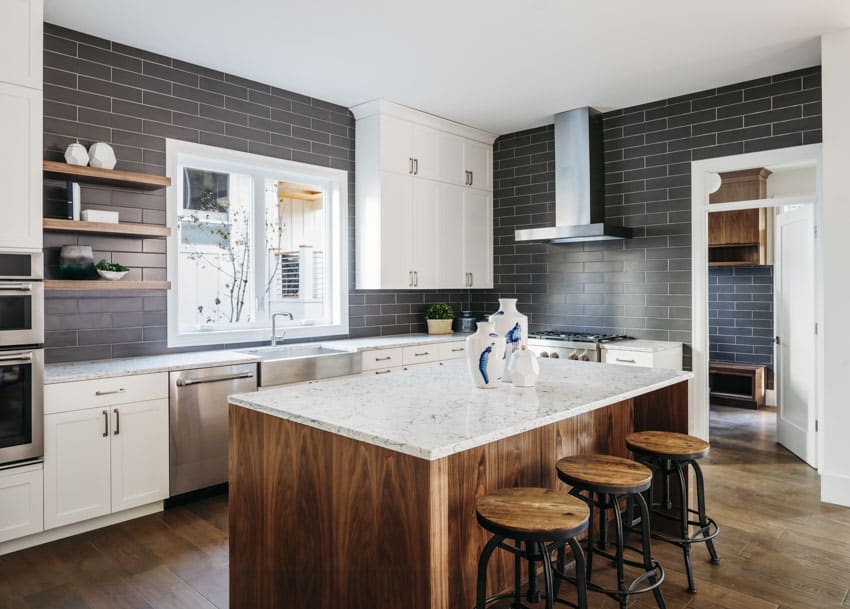 Contemporary kitchen with marble countertop, black subway tile backsplash, range hood, window, floating shelves, cabinets, and bar stools
