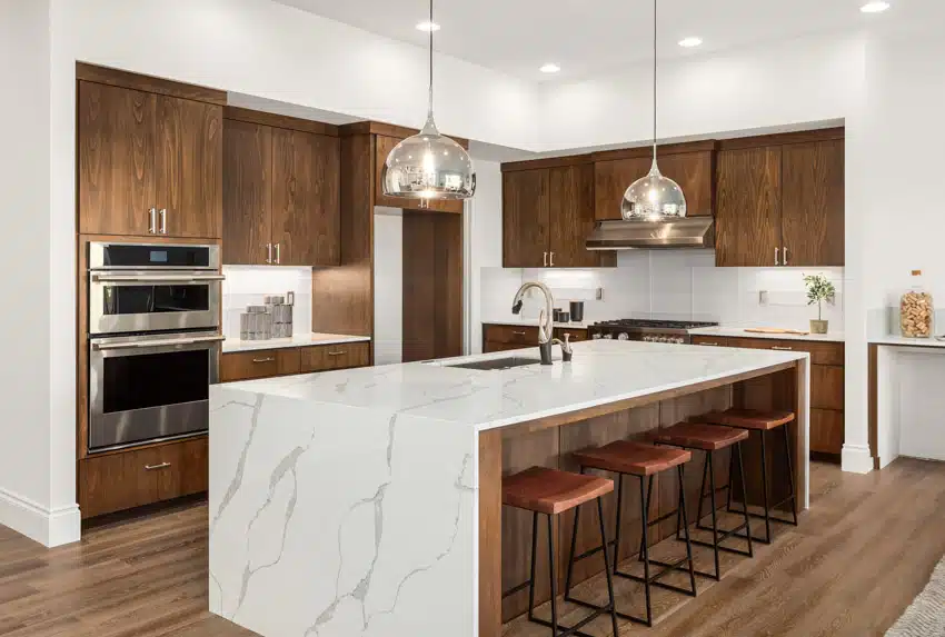 Contemporary kitchen with quartz countertop, bar stools, island, pendant lights, wood cabinets, oven, and wooden flooring