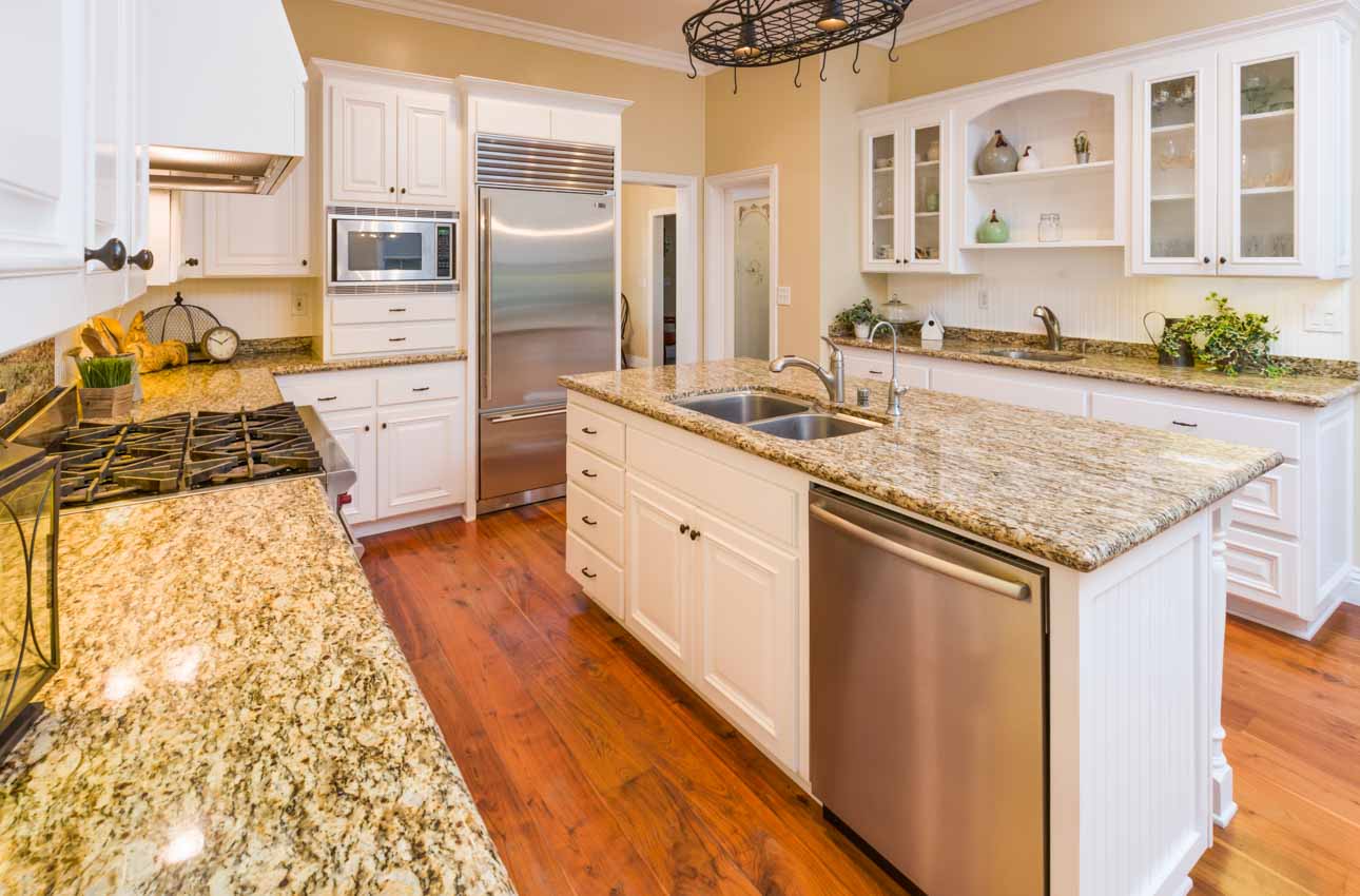 Contemporary kitchen with white cabinets, Santa Cecilia granite countertops, island, stove, oven, refrigerator, and chandelier