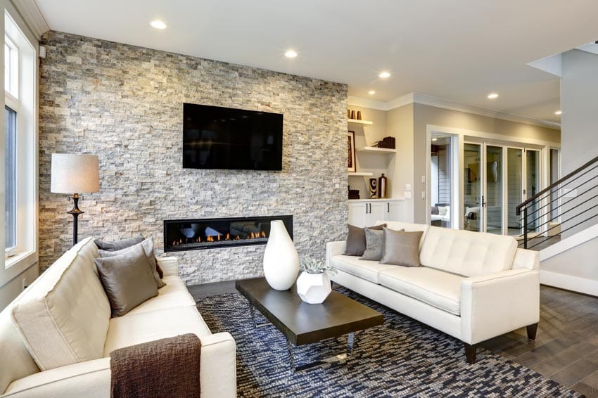 Grey accented room with stone fireplace, white sofa, television, floor lamp