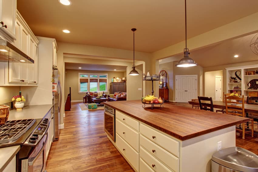 Craftsman kitchen with teak countertop, island, pendant lights, white cabinets, wood floors, and stove