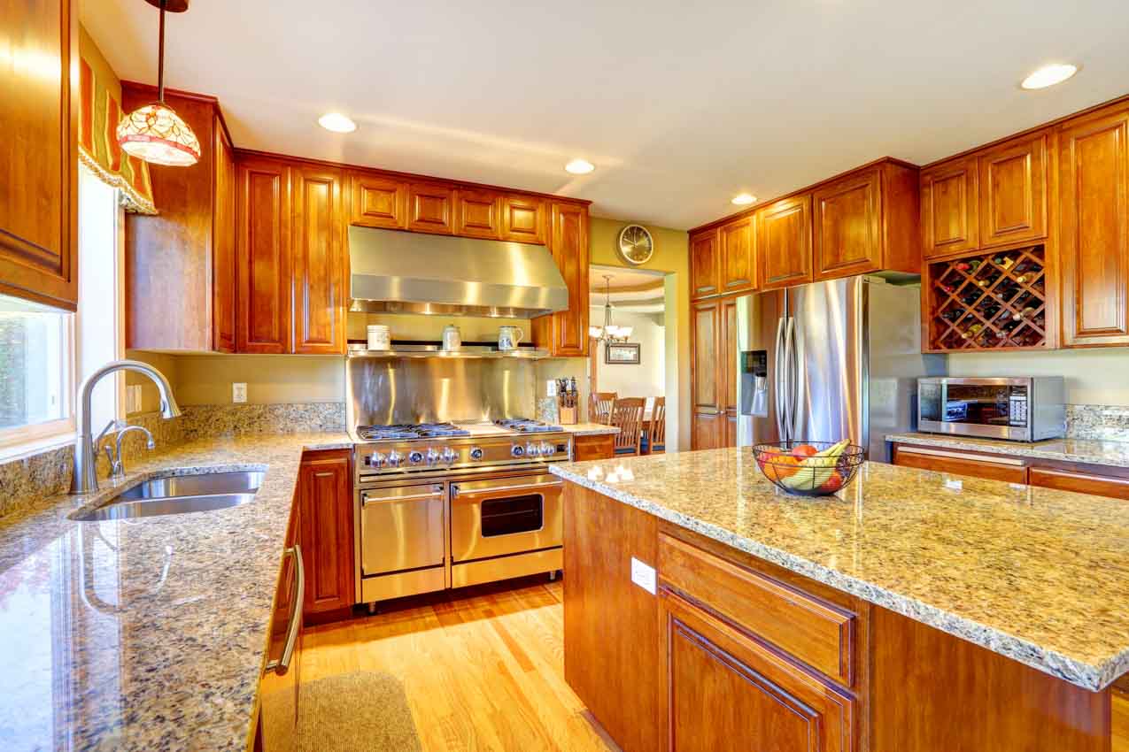 Craftsman kitchen with wood cabinets, island, granite counter, oven, range hood, sink, faucet, and pendant light
