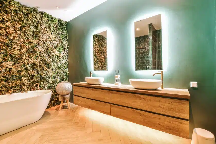 Dark green bathroom with mirrors, floating vanity, sinks, faucets, accent lights, leaf accent wall, and bathtub