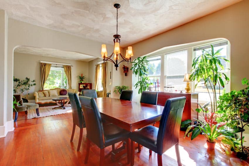 Dining room with cherry wood table, chairs, windows, wood flooring, couch, curtains, and indoor plants