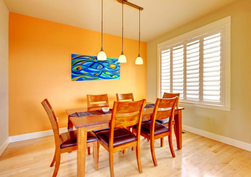 Dining room with satin Indian wood table, chairs, pendant lights, window, shutters, and wooden flooring