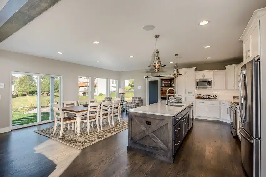 Farmhouse kitchen with dining table chairs, dark walnut floors, island, countertops, cabinets, windows, and pendant lights