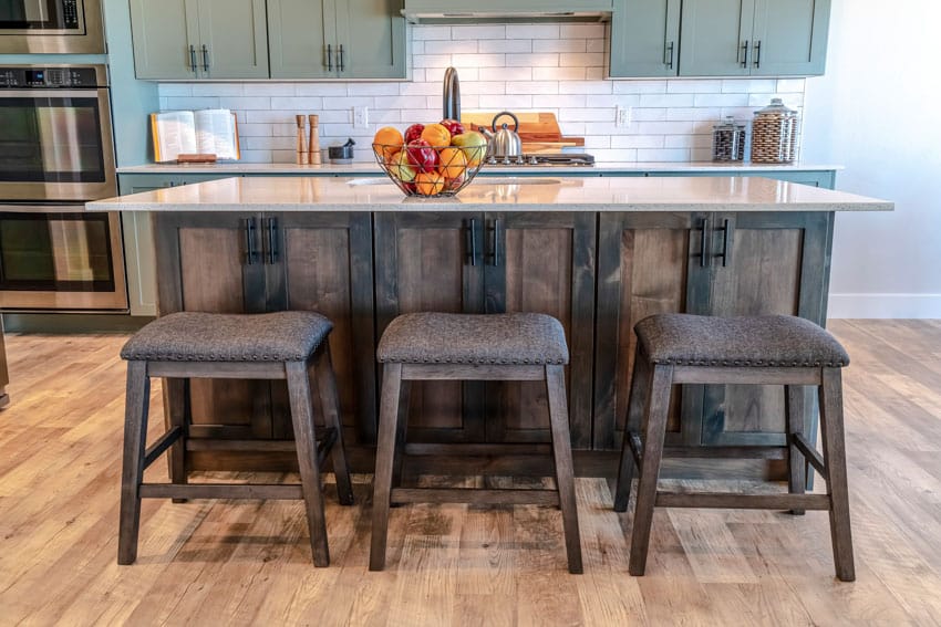 Kitchen with natural maple wood floor, bar stools, island, countertop, green cabinets, and subway tile backsplash