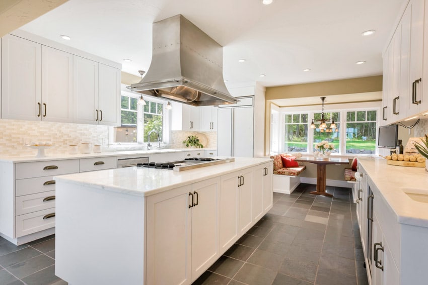 White farmhouse kitchen with, dining nook, island, white cabinets, slate tile floors, and windows