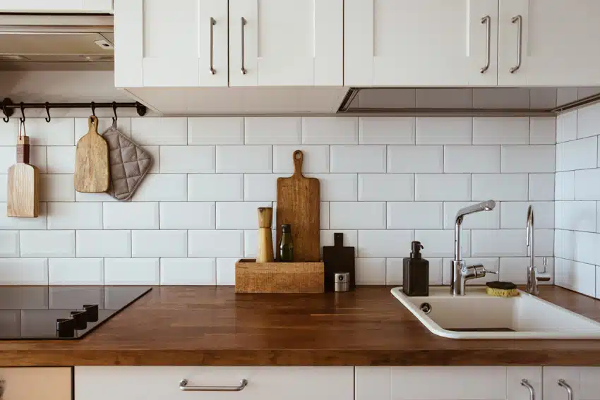 Farmhouse kitchen with teak butcher block countertop, white cabinets, and subway tile backsplash