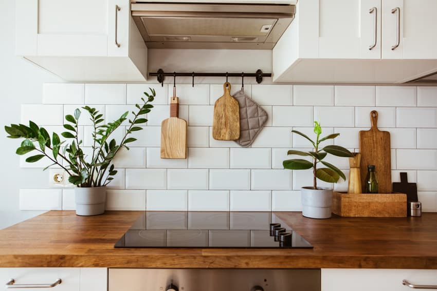 Farmhouse kitchen with teak countertop, induction stove, subway tile backsplash, range hood, and cabinets