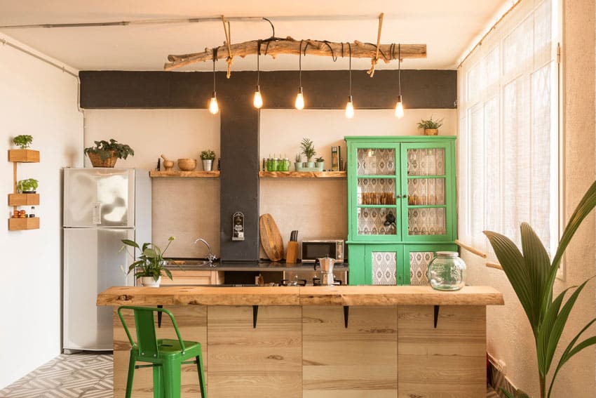 Farmhouse kitchen with wallpaper inside green glass cabinet, wood island, floating shelves, pendant lights, refrigerator, chair, window, and curtains