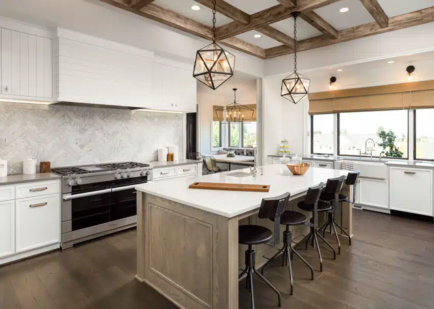 Farmhouse kitchen with, island, countertops, cabinets, range hood, marble herringbone backsplash, ceiling beams, windows, and pendant lights