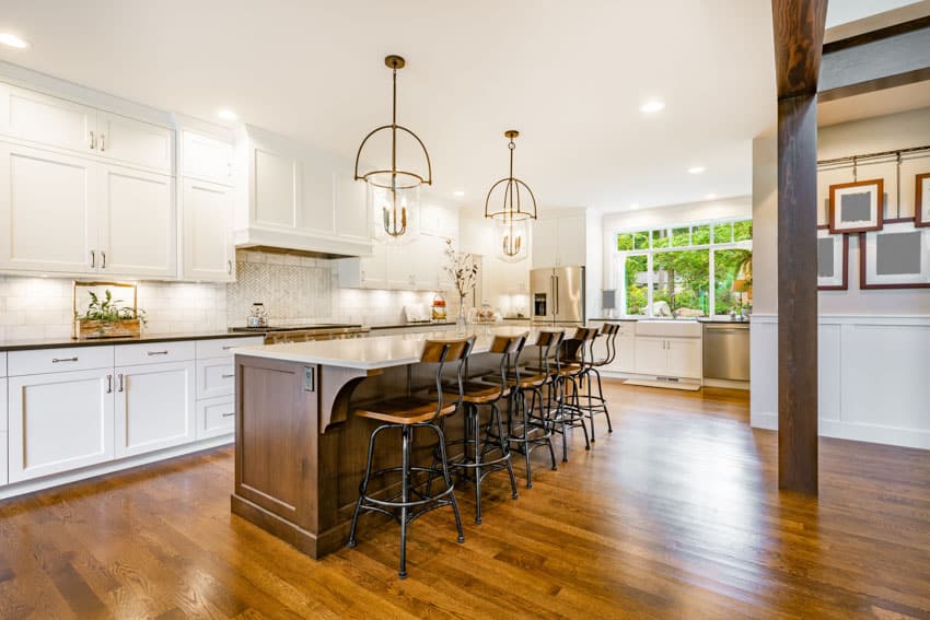 Farmhouse kitchen with wood flooring, island, high chairs, white cabinets, pendant lights, and range hood