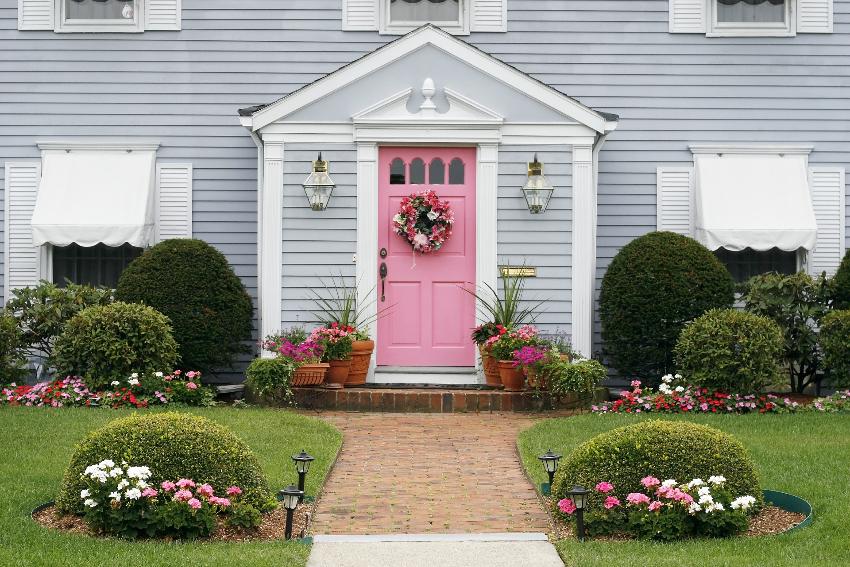 Front of beautiful gray house with blush pink door paint and garden