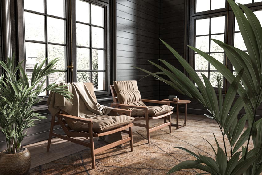 Living room with natural wood chairs, black framed windows, large floor rug, and indoor plants