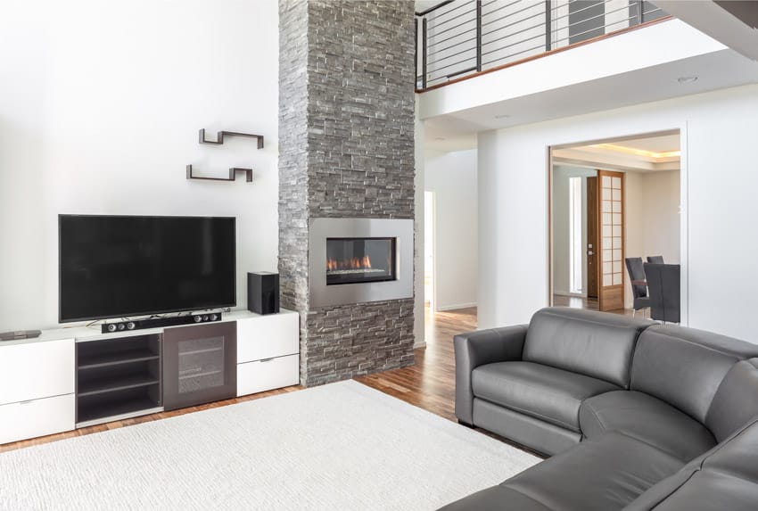 Living room with ledger stone tile wall, television, leather couch, TV stand, and floor rug