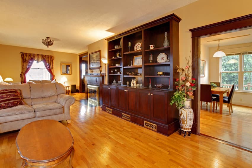 Living room with mahogany Indian wood bookshelf, coffee table, couch, window, curtains, floor vase, and wooden flooring
