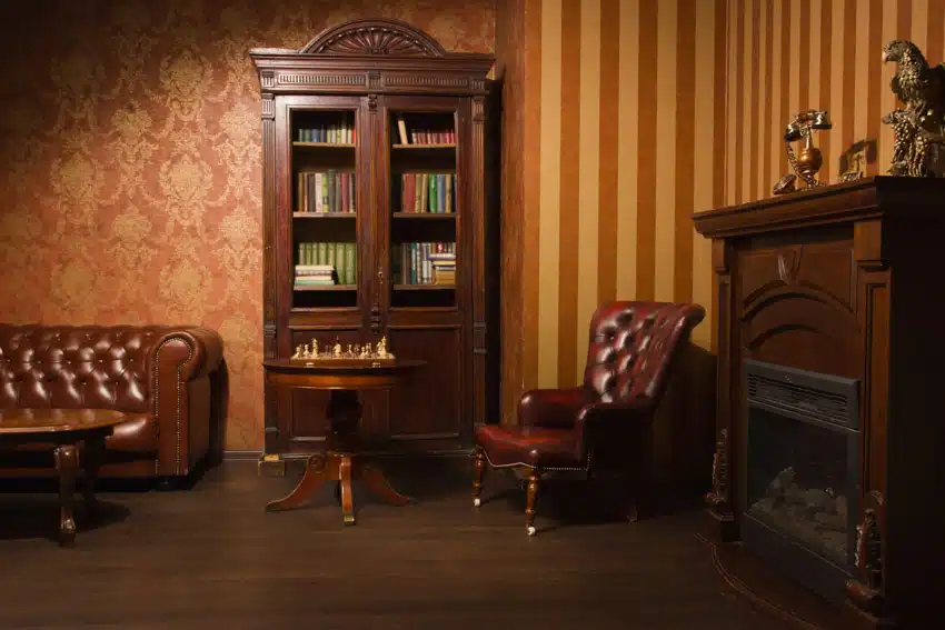 Living room with regency style brown leather chair, couch, glass cabinet, round table, wallpaper, and fireplace