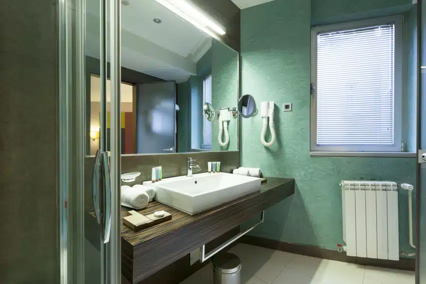 Mint green bathroom with heater, floating vanity, sink, faucet, mirror, accent lighting fixture, tile floor, and window
