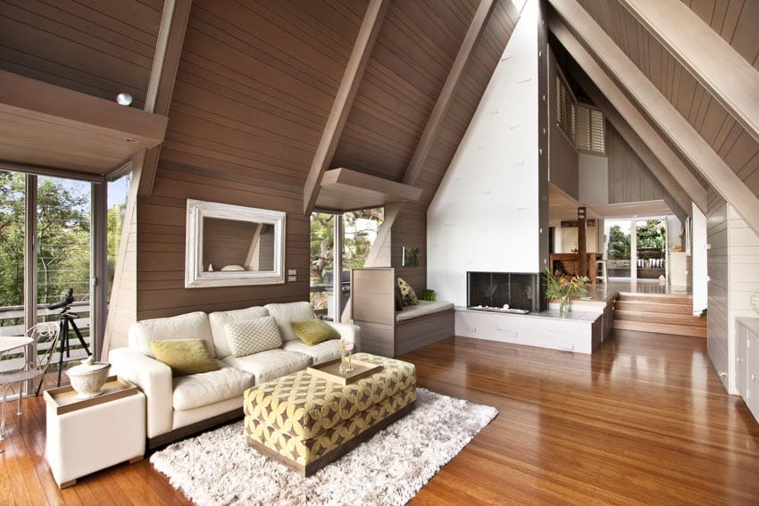Modern cottage living room interior with finished wood floors, beadboard ceiling, sofa, ottoman, coffee table, glass door, and fireplace