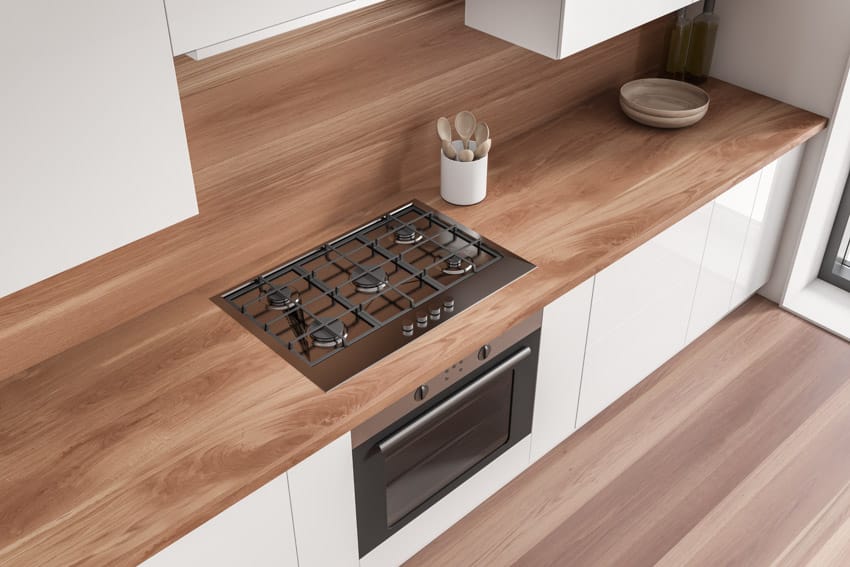 Modern kitchen with Burmese teak wood countertop, oven, and white cabinets