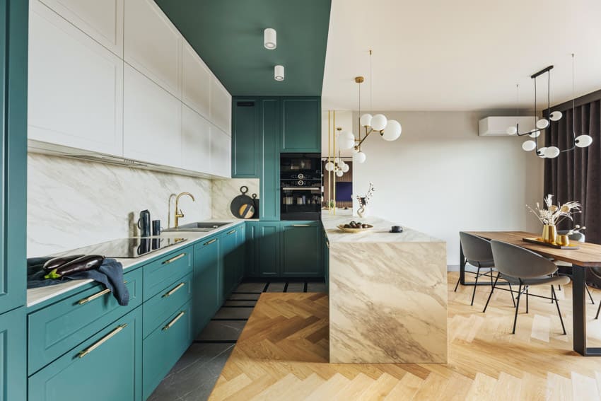 Modern kitchen with green cabinets, peninsula, countertops, marble backsplash, and wood herringbone floor