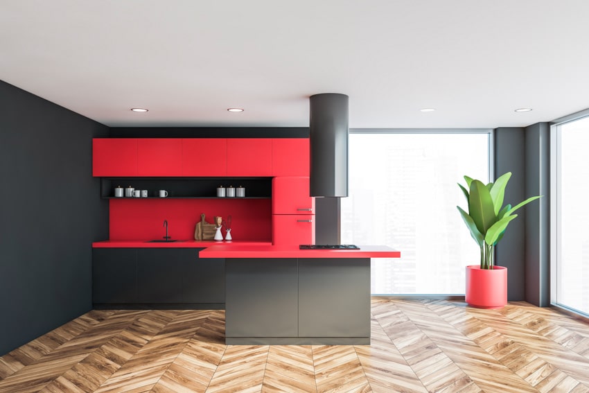 Modern kitchen with island, wood flooring, red quartz countertop, range hood, red backsplash, indoor plant, and windows