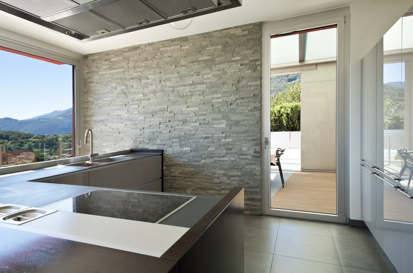 Modern kitchen with ledger stone wall, countertop, sink, faucet, range hood, and windows